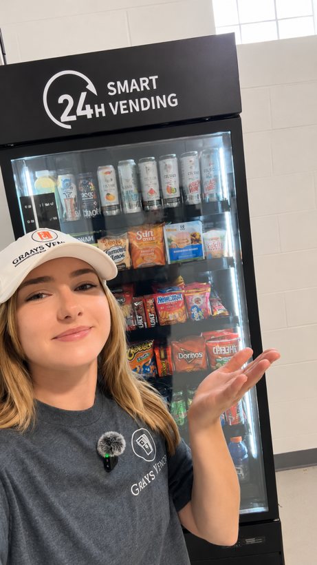 Briana in her Grays Vending polo in front of one of her stocked machines